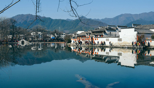 A scenic view of Hongcun across a body of water at the base of Mount Huangshan